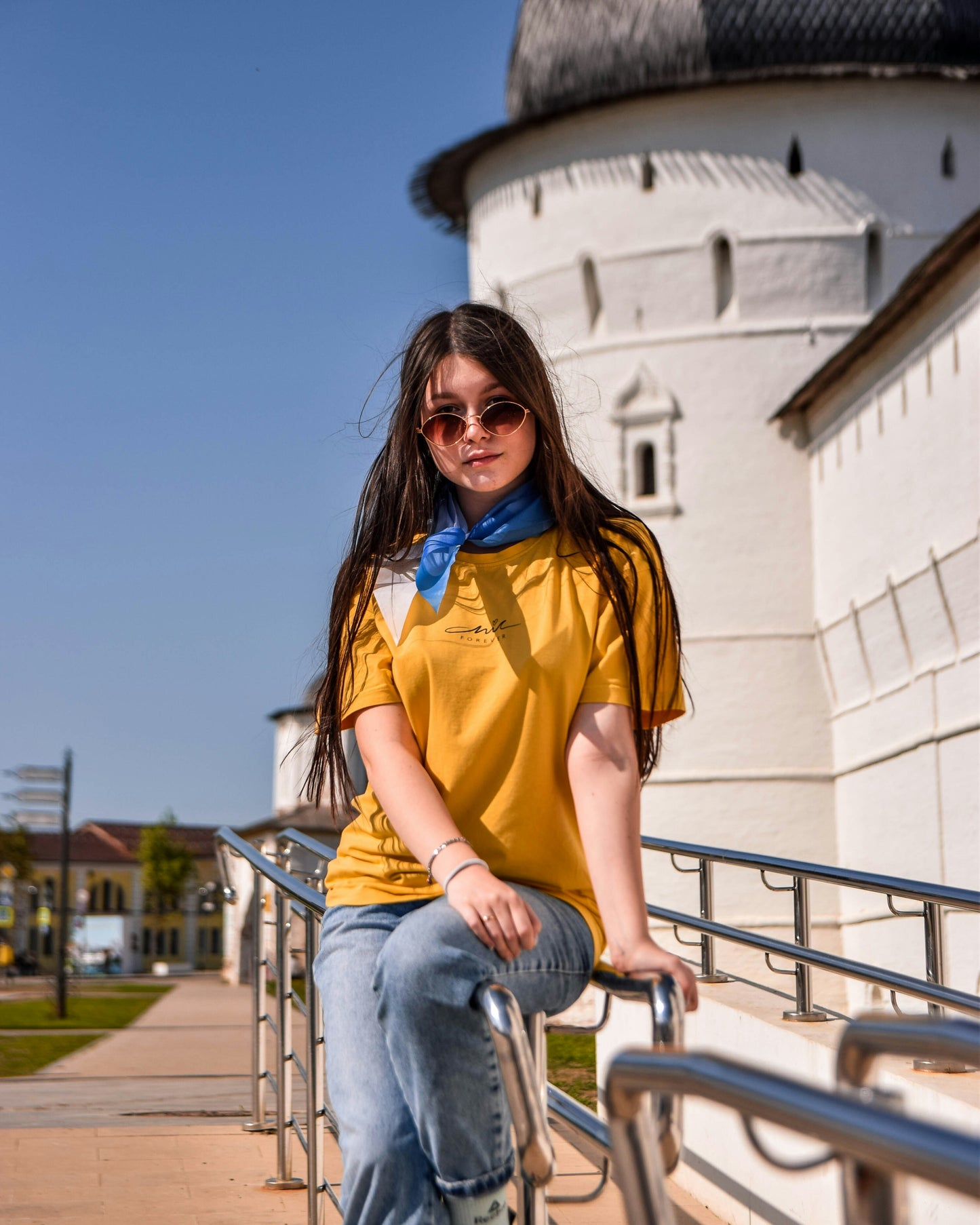 Woman in yellow shirt and sunglasses sitting on a railing with a historical building in the background
